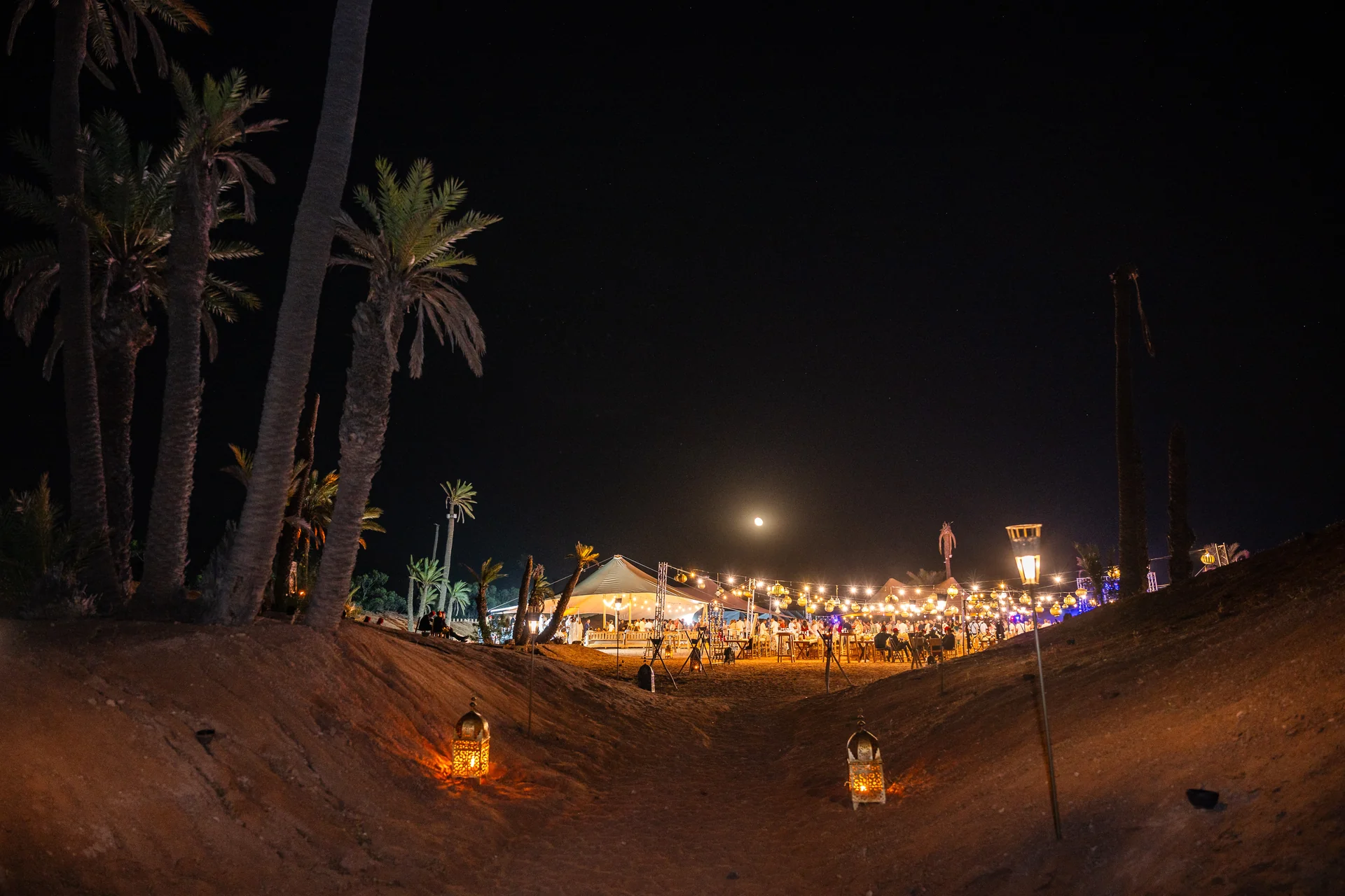 Soirée de séminaire incentive dans le désert de Marrakech, tente caïdale illuminée et lanternes orientales sous la pleine lune